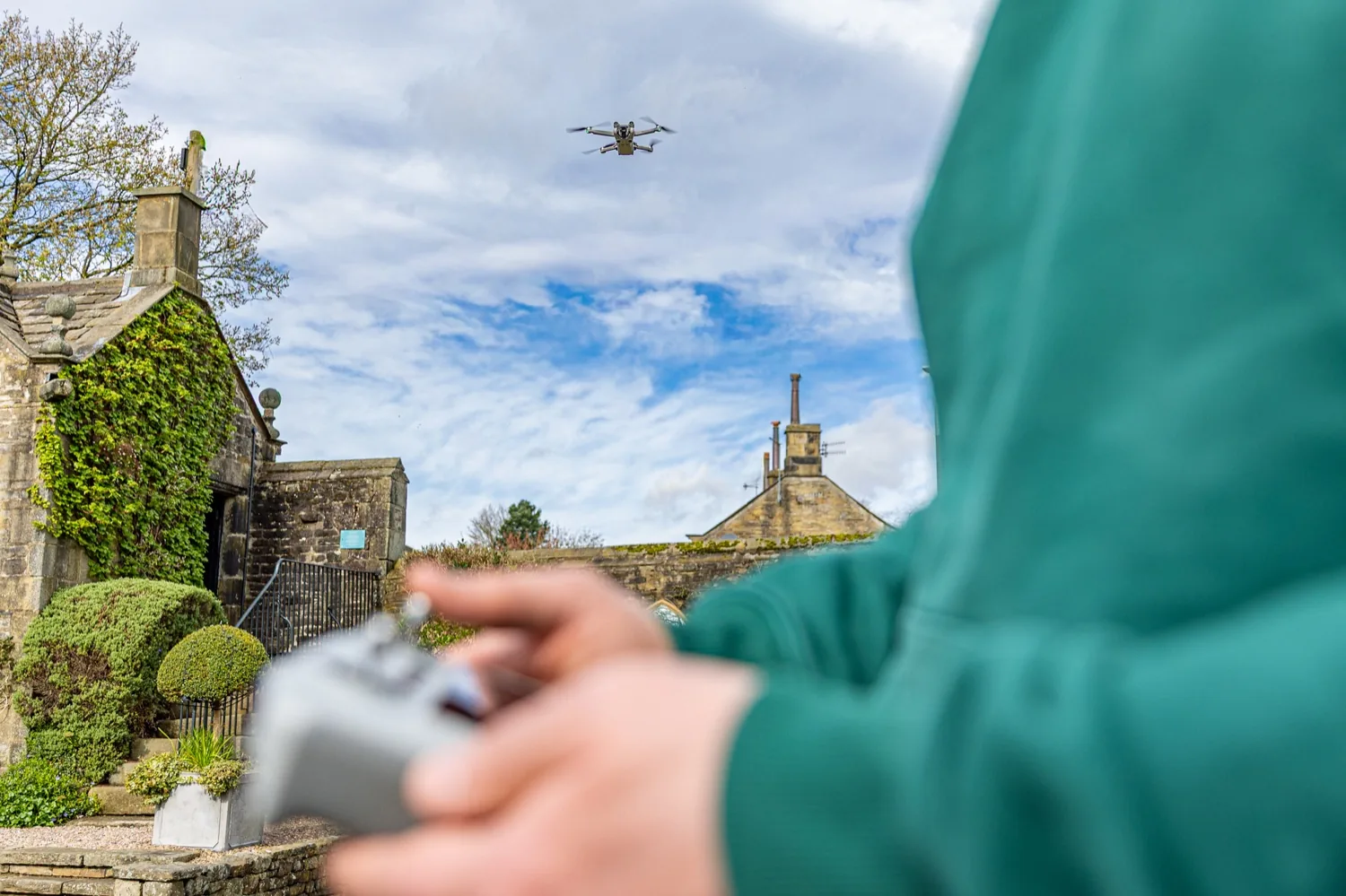 A Halizona drone in the air over a stone building in Yorkshire, the pilot in the foreground