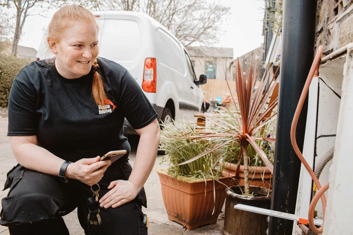 Fay Dolphin of Dolphin Heating checking a boiler flue at a customer&rsquo;s house, her van parked behind her